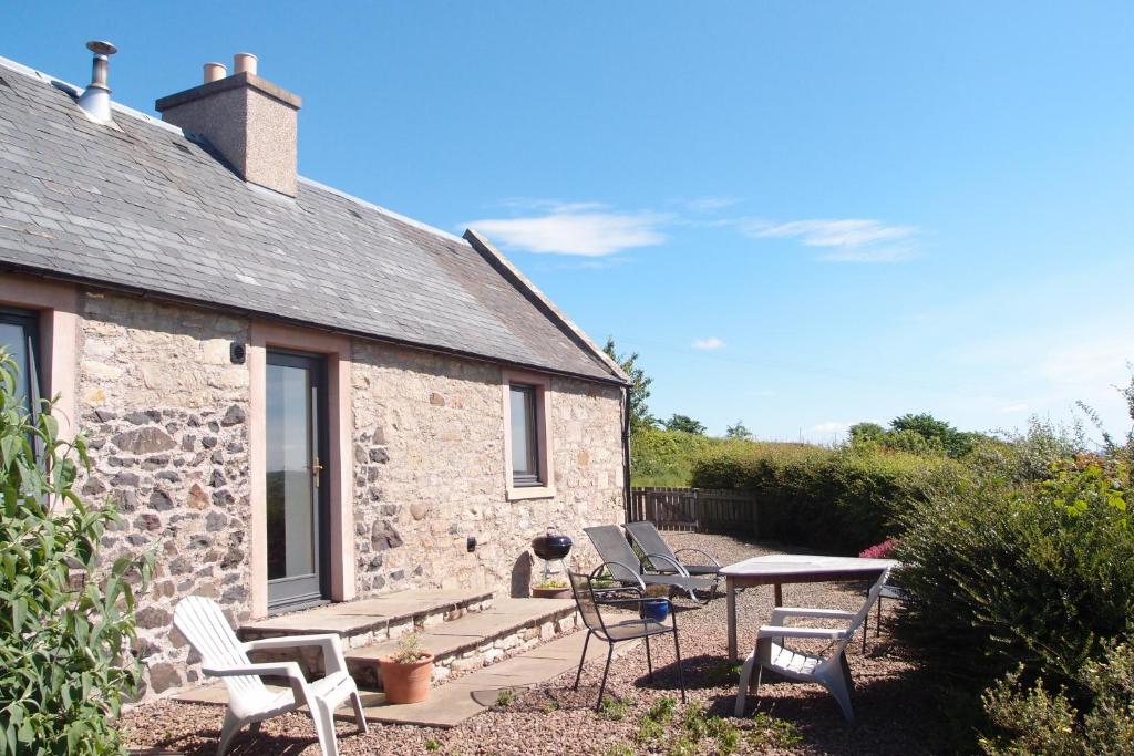 a stone cottage with chairs and a table on a patio at Cocklekitty Cottage in Kelso