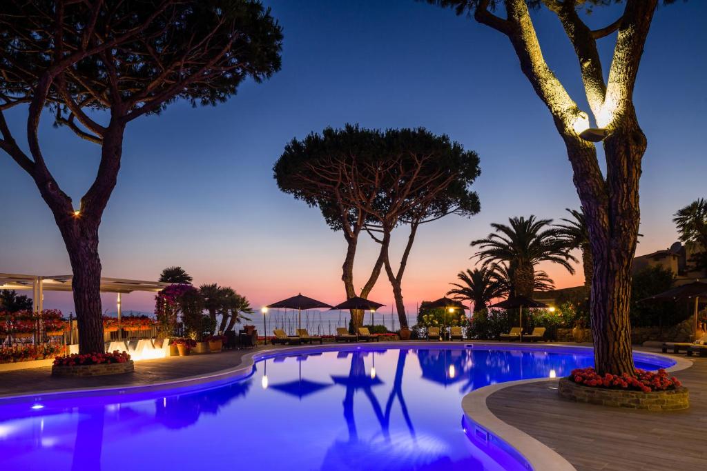 una piscina por la noche con árboles y luces en Cala del Porto Resort, en Punta Ala