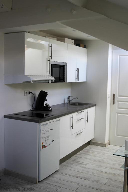 une cuisine avec des armoires blanches et un chat noir sur le comptoir dans l'établissement Beau Studio Nice, à Nice