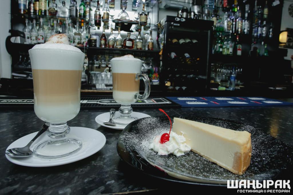 dos cócteles y un trozo de tarta de queso en un bar en Shanyrak Hotel en Temirtaū