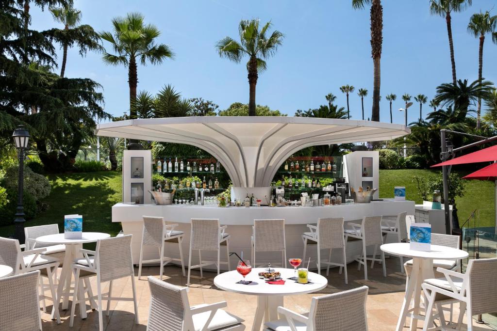 a restaurant with white tables and chairs and a bar at Hôtel Barrière Le Majestic Cannes in Cannes
