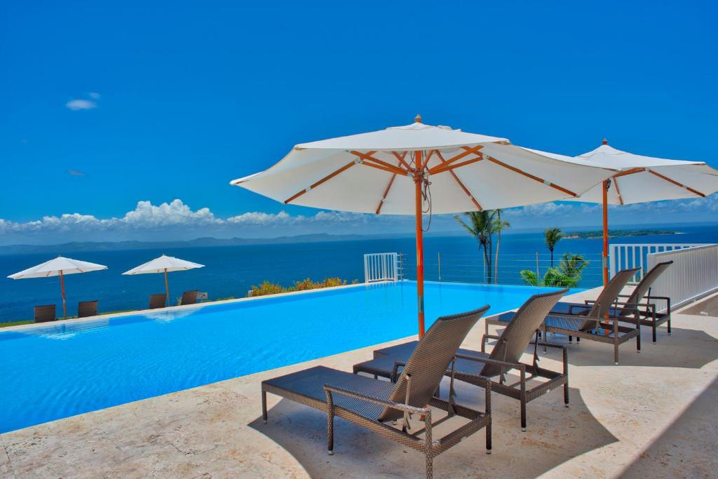 a pool with chairs and umbrellas and the ocean at Xeliter Vista Mare, Samana in Santa Bárbara de Samaná