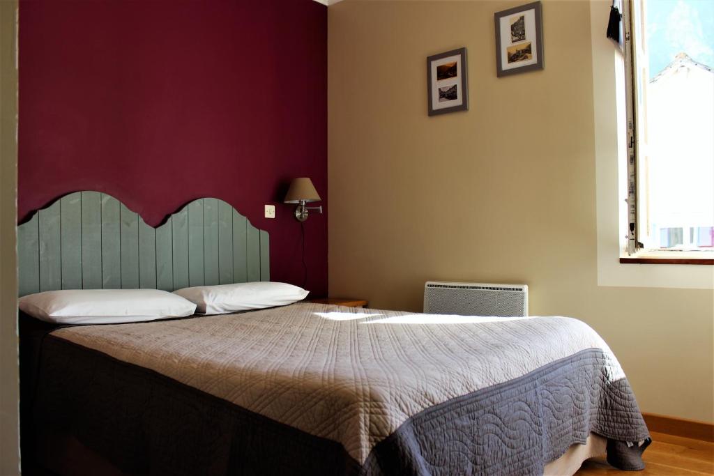 a bedroom with a large bed with a red wall at Hôtel BURLATIS in Sainte-Énimie