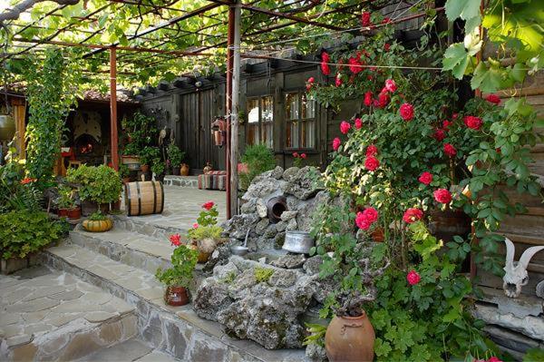 un jardin avec des roses et une cascade en pierre dans une serre dans l'établissement Guest House Polah Ot Minaloto, à Zheravna