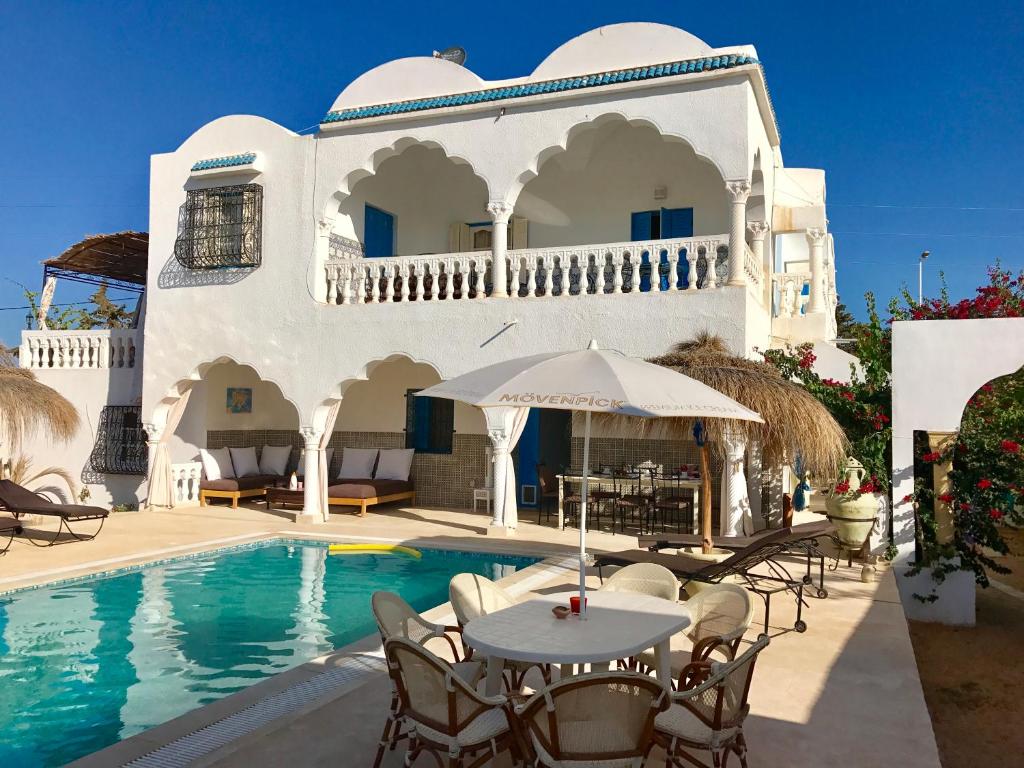 a villa with a swimming pool and tables and chairs at Menzel Churasco Djerba in Aghīr