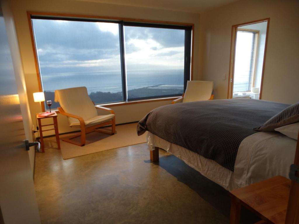 a bedroom with a bed and two chairs and a large window at Big Sky Nelson Luxury Eco B&B in Nelson
