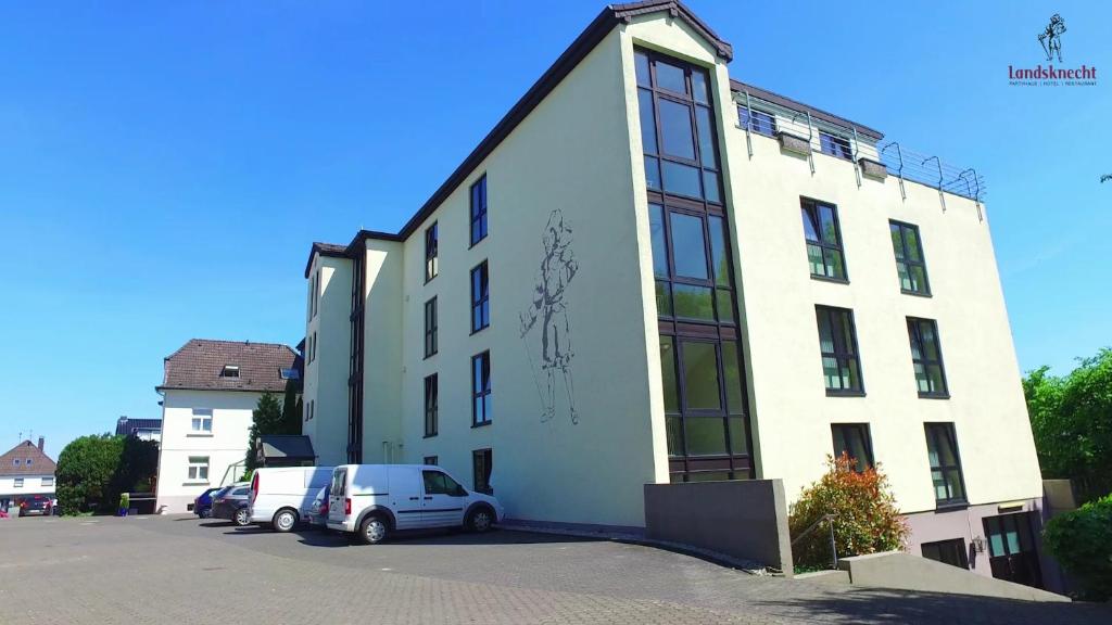 un edificio blanco con coches estacionados en un estacionamiento en Hotel Landsknecht, en Uckerath