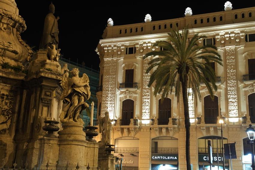 a building with a statue and a palm tree in front of it at Palazzo Moncada Apartment in Palermo