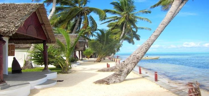 a beach with palm trees and a building and the ocean at Hotel Club Paradise in Sainte Marie