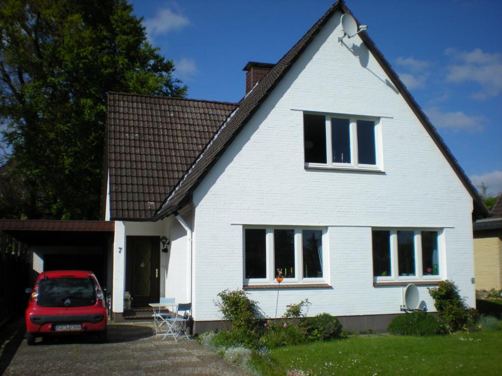une maison blanche avec une voiture rouge garée devant dans l'établissement Ferienwohnung Lohmann, à Fleckeby