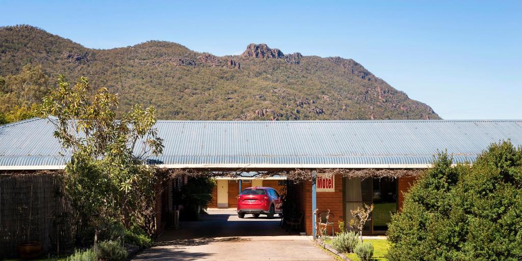 un coche rojo estacionado frente a una casa con una montaña en Kookaburra Motor Lodge en Halls Gap