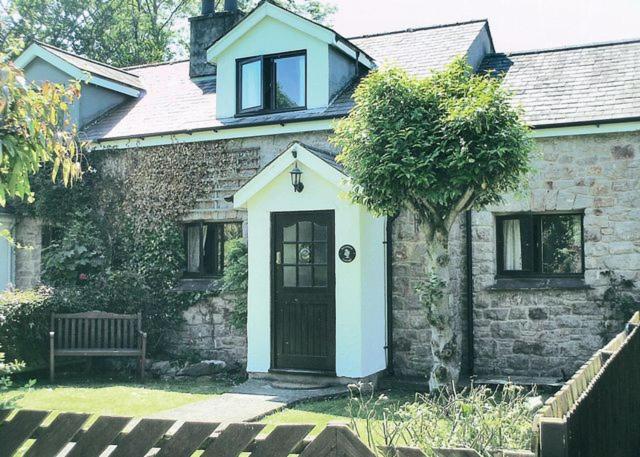 een stenen huis met een zwarte deur en een boom bij Sycamore Cottage in Conwy