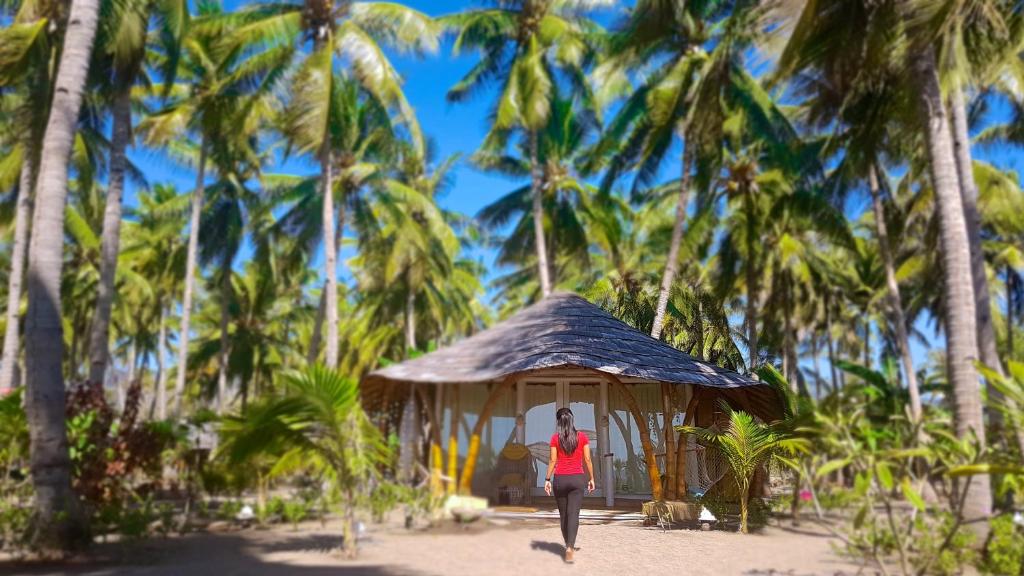a woman walking past a small hut in front of palm trees at Coconut Garden Beach Resort in Maumere
