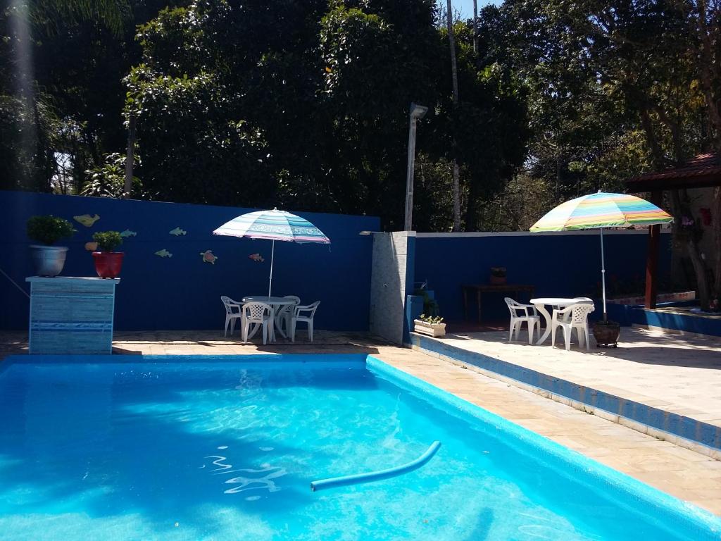 a swimming pool with two umbrellas and a table and chairs at Pousada Albergue Kafundó in Jaguariúna