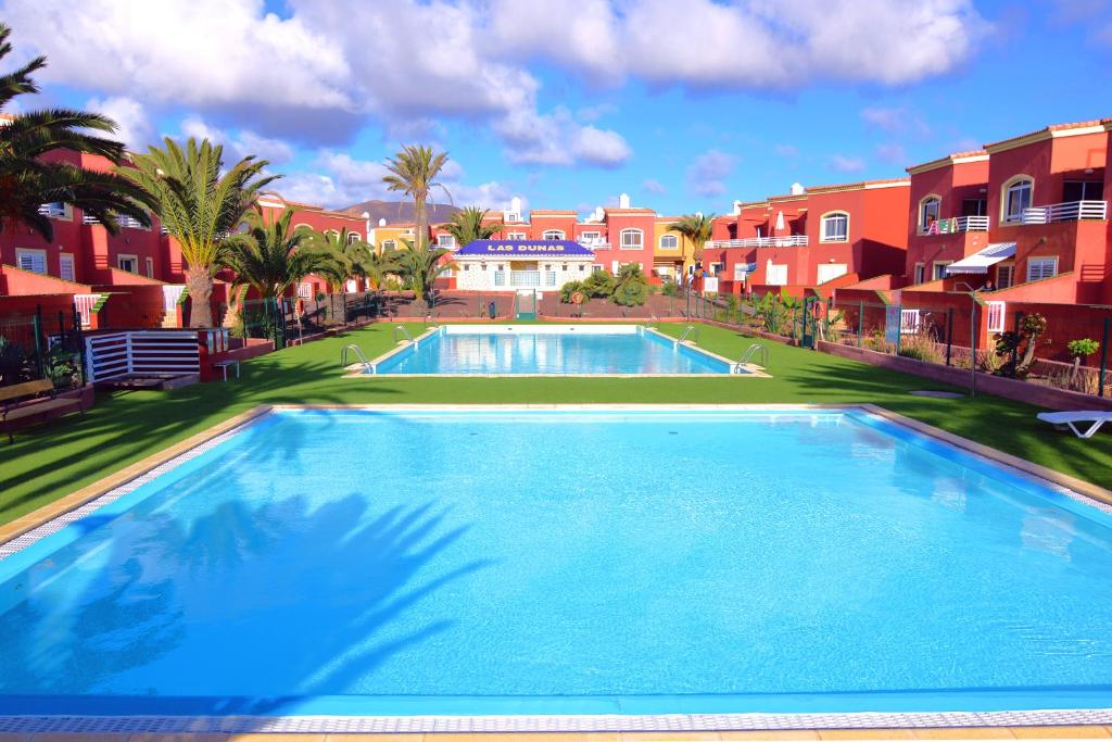 a large swimming pool with palm trees and buildings at Kalmahouse in Corralejo