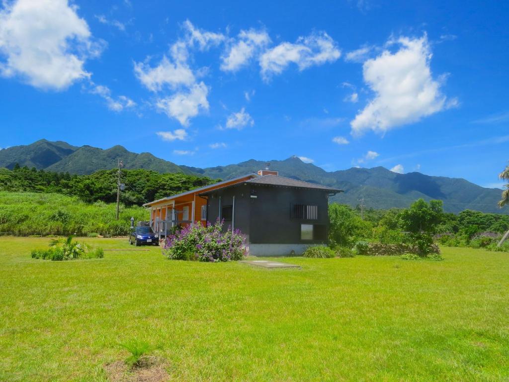 a house in a field with mountains in the background at Cottage Orange House Yakushima in Yakushima