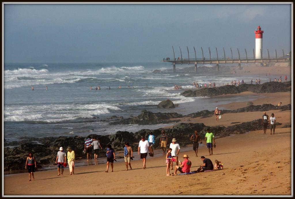 Un grupo de personas caminando por una playa con un faro. en 6 Ipanema Beach, en Durban