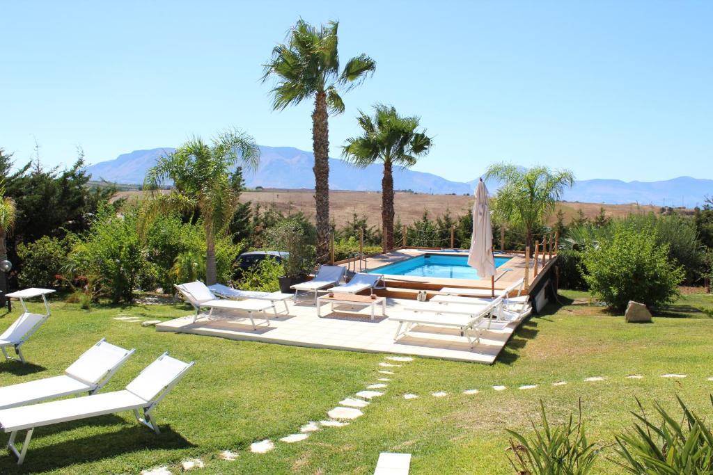 une cour avec une piscine, des chaises et des palmiers dans l'établissement Isola del sole, Appartamenti con piscina, à Balestrate