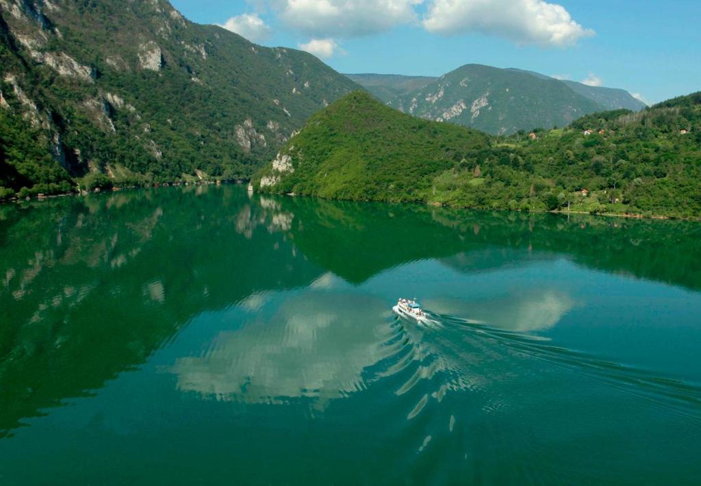 a boat in the middle of a lake with mountains at Viola i Detelina Apartments in Perućac