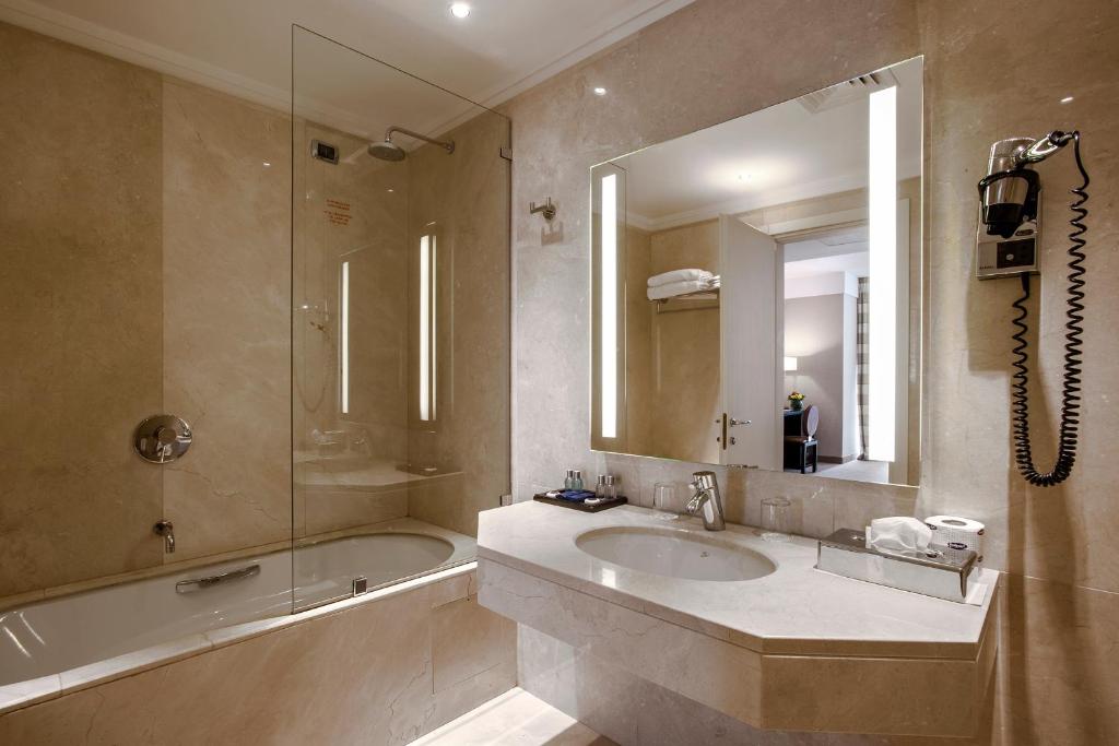 W łazience znajduje się umywalka, wanna i lustro. w obiekcie Ergife Palace Hotel w Rzymie