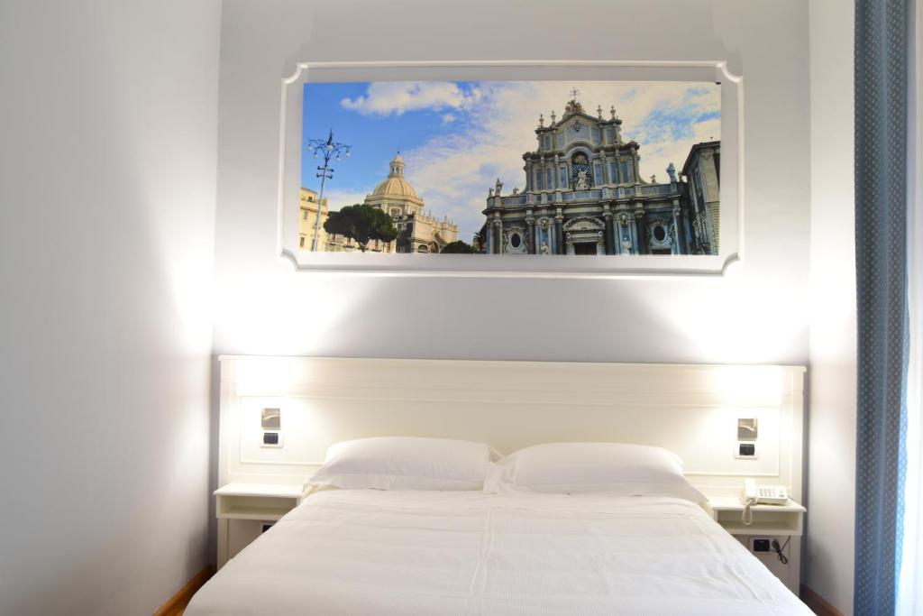 a bedroom with a white bed with a picture on the wall at Hotel Centrum in Catania