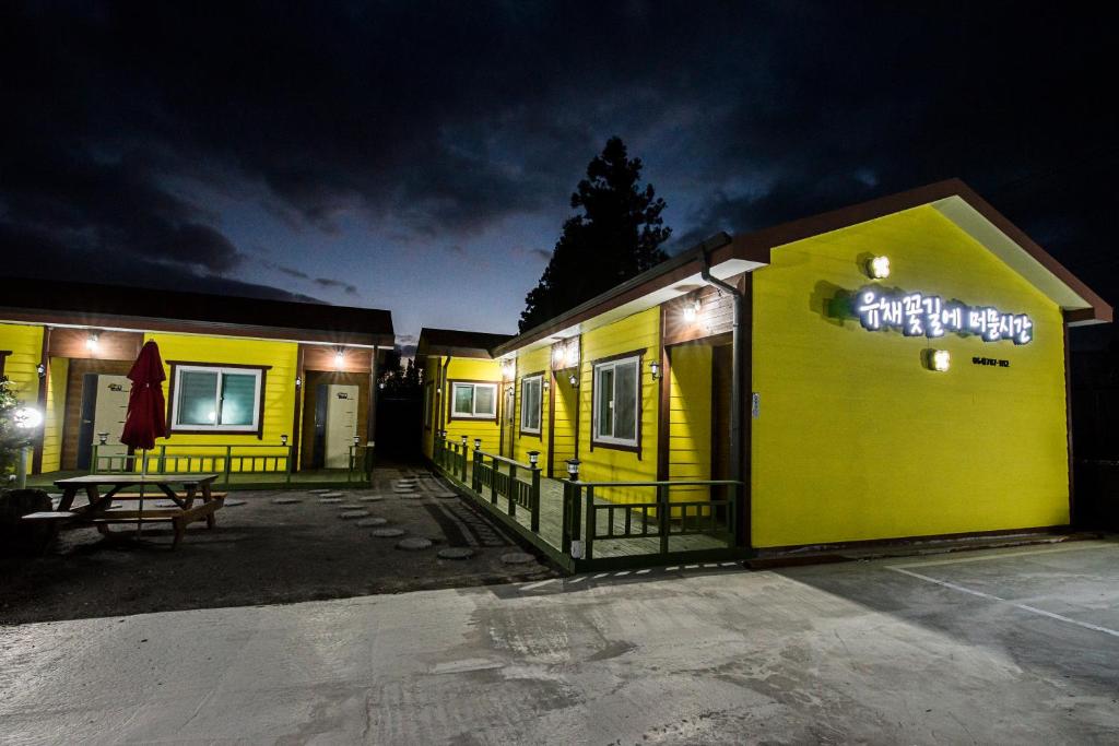 un edificio amarillo con un cartel en él por la noche en Brassica Flower Pension en Seogwipo