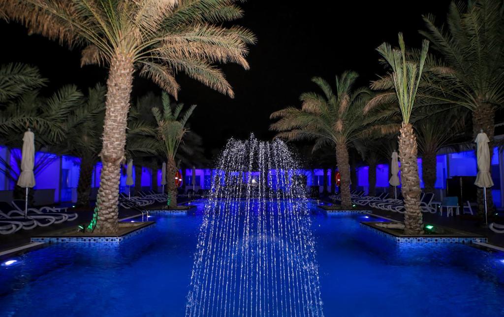 a pool with blue lights in front of palm trees at Fujairah Hotel & Resort in Fujairah