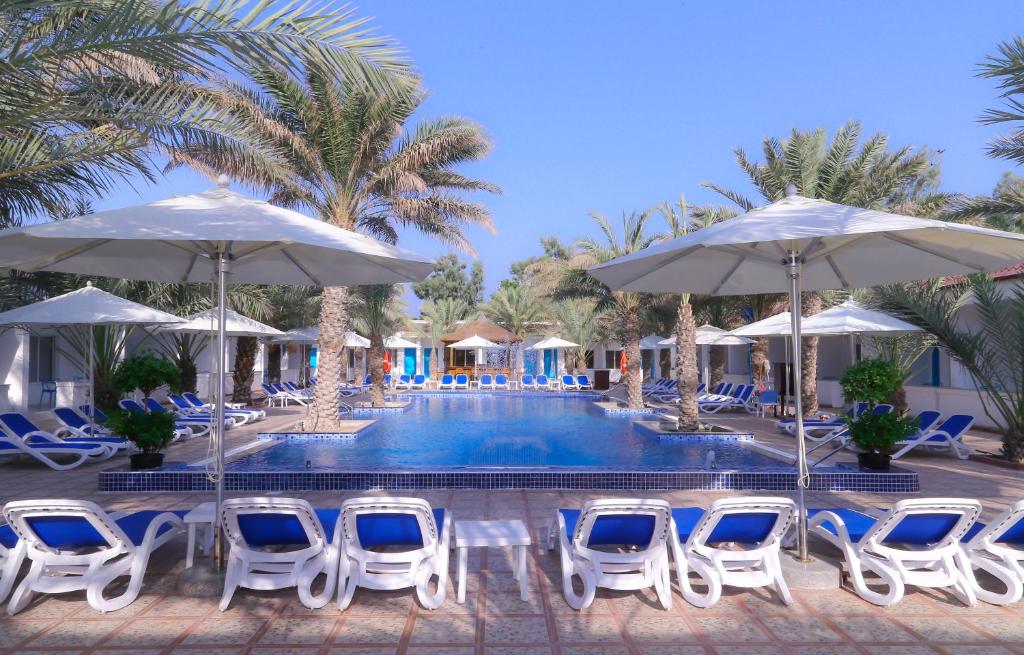 a pool with blue and white chairs and umbrellas at Fujairah Hotel & Resort in Fujairah