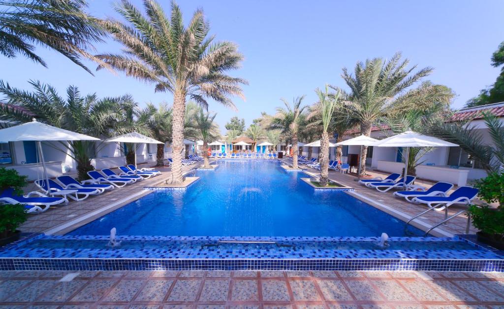 una piscina in un resort con sedie e palme di Fujairah Hotel & Resort a Fujaira