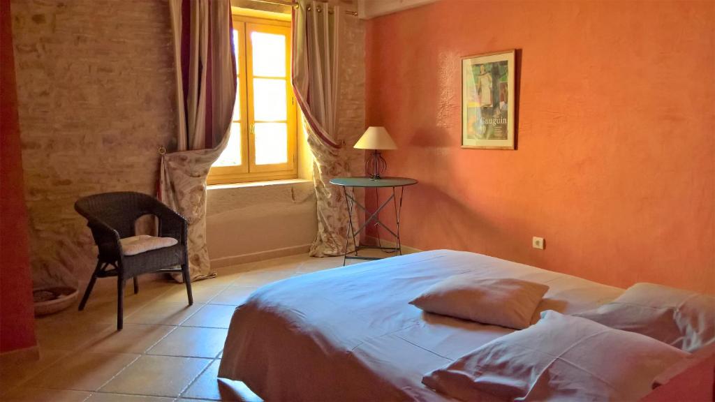 a bedroom with a bed and a chair and a window at Le Clos des Pierres Dorées in Theizé