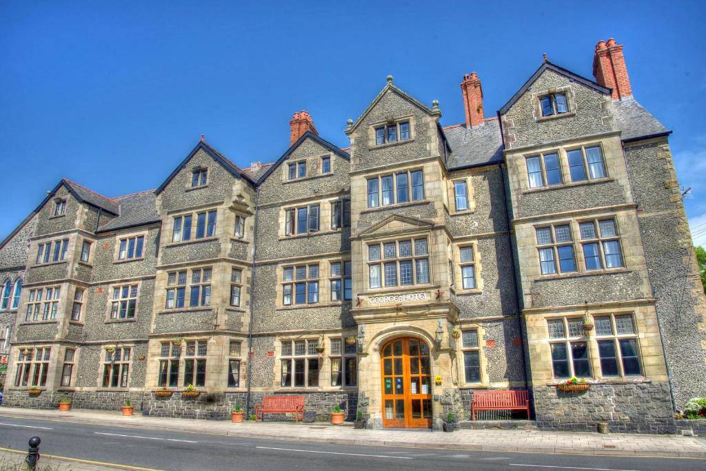 un antiguo edificio de piedra al lado de una calle en George IV Hotel, en Criccieth