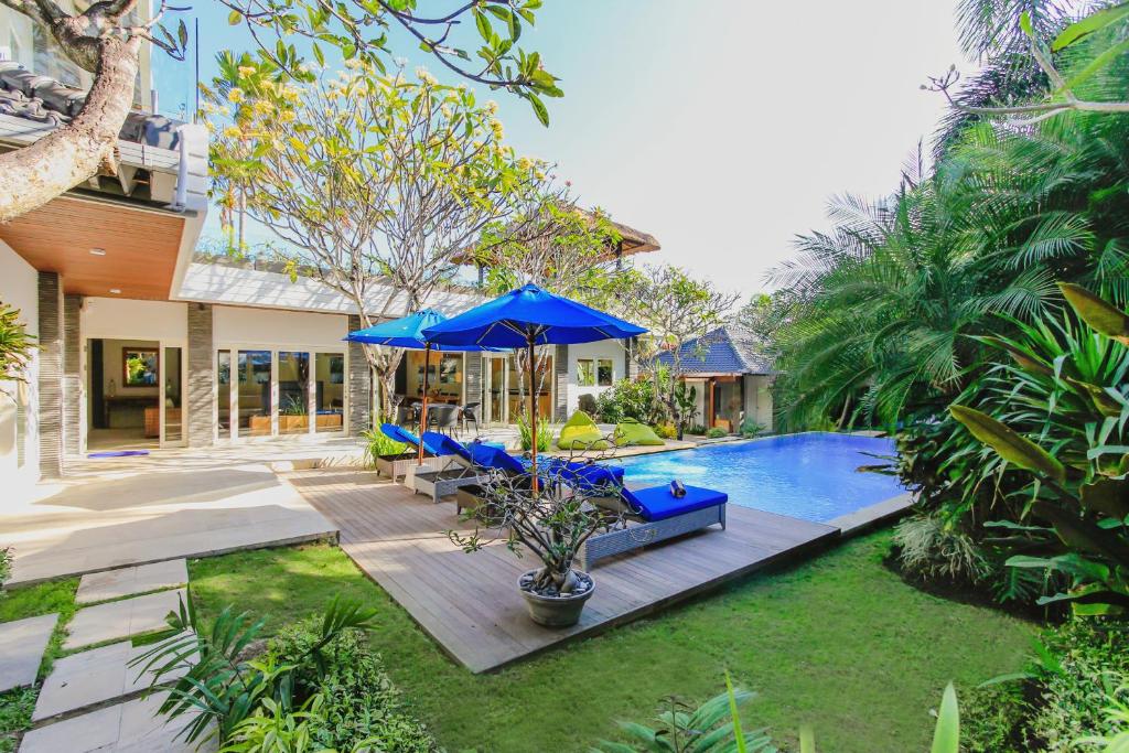 um quintal com uma piscina com cadeiras azuis e um guarda-sol em Villa La Luvier em Canggu