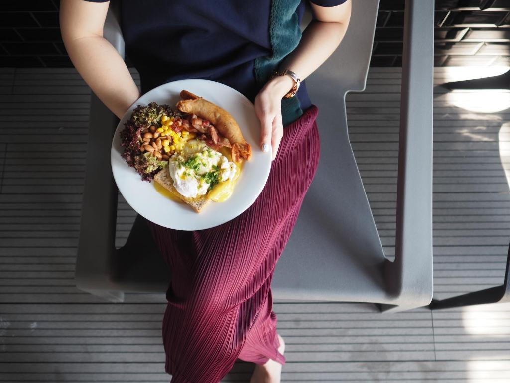 A guest holding a breakfast plate beside poolside-style loungers on a slatted deck.