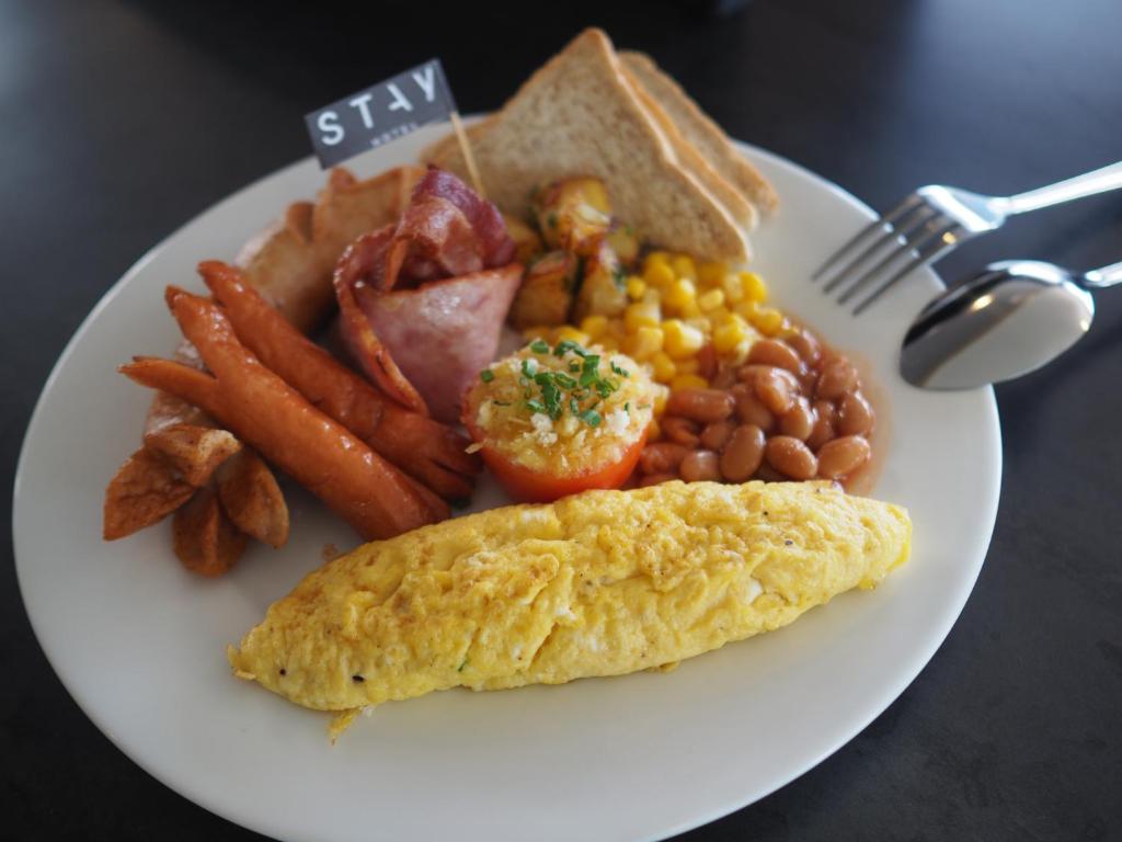 A full cooked breakfast plate with omelette, bacon, sausages, toast, beans, potatoes, and vegetables.