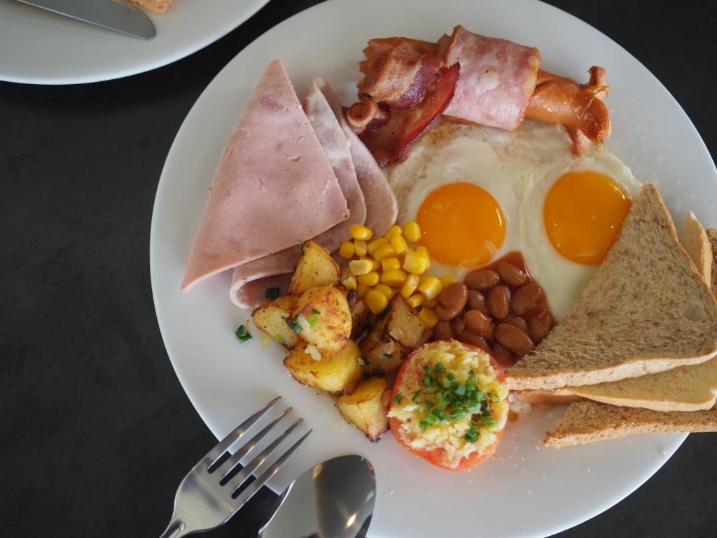 A cooked breakfast plate with fried eggs, bacon, ham, toast, beans, corn, and potatoes.