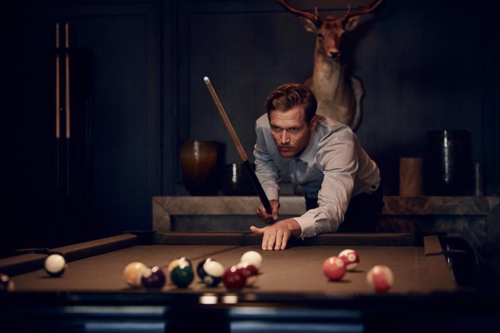 a man standing over a pool table with a cue at Apogée Courchevel, Oetker Hotels in Courchevel