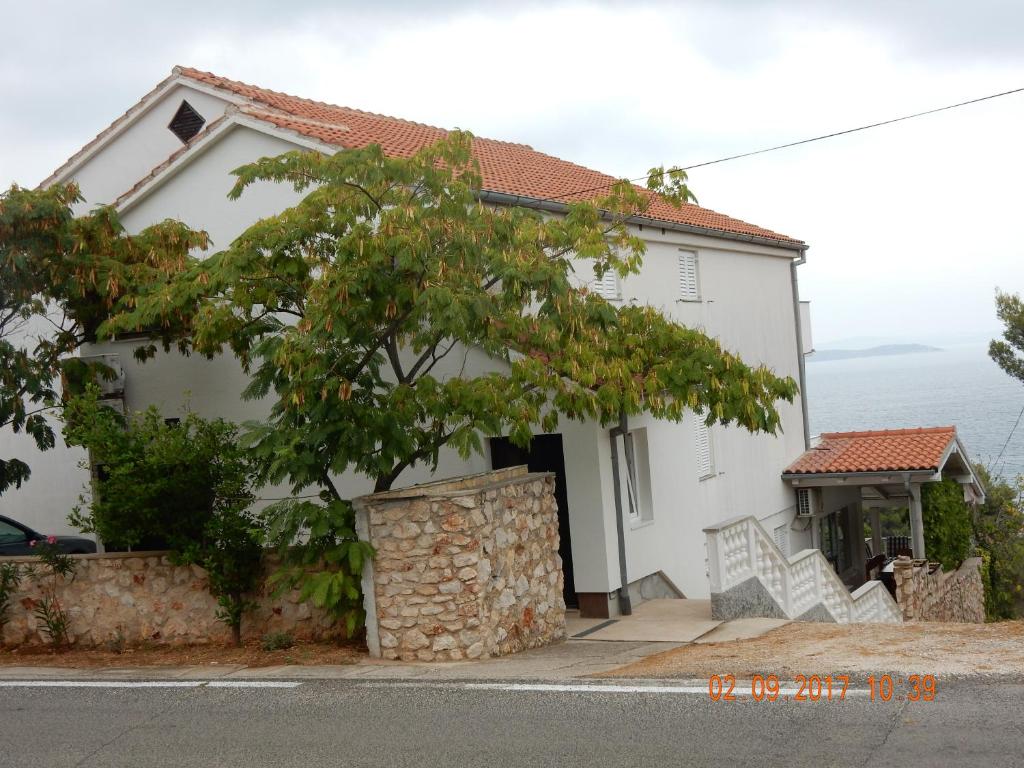ein weißes Haus mit einem Baum davor in der Unterkunft Apartments Mandolina - Hiša na samem s pogledom na morje in Žman