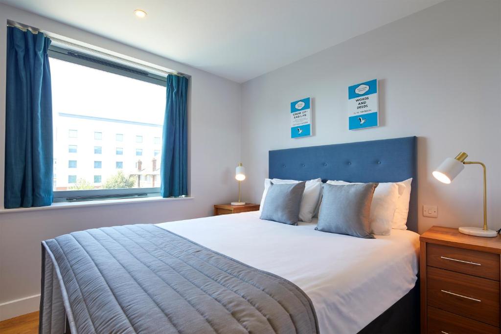 um quarto com uma cama com uma cabeceira azul e uma janela em HQ Aparthotel Farnborough em Farnborough