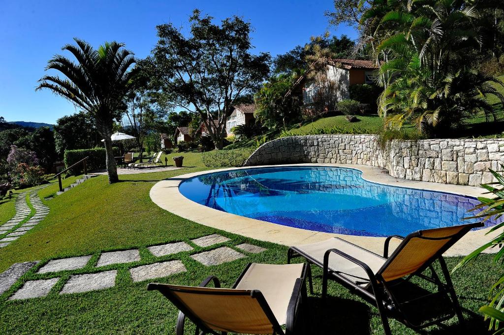 a swimming pool with two chairs and a stone wall at Pousada Recanto das Araras in Araras Petropolis