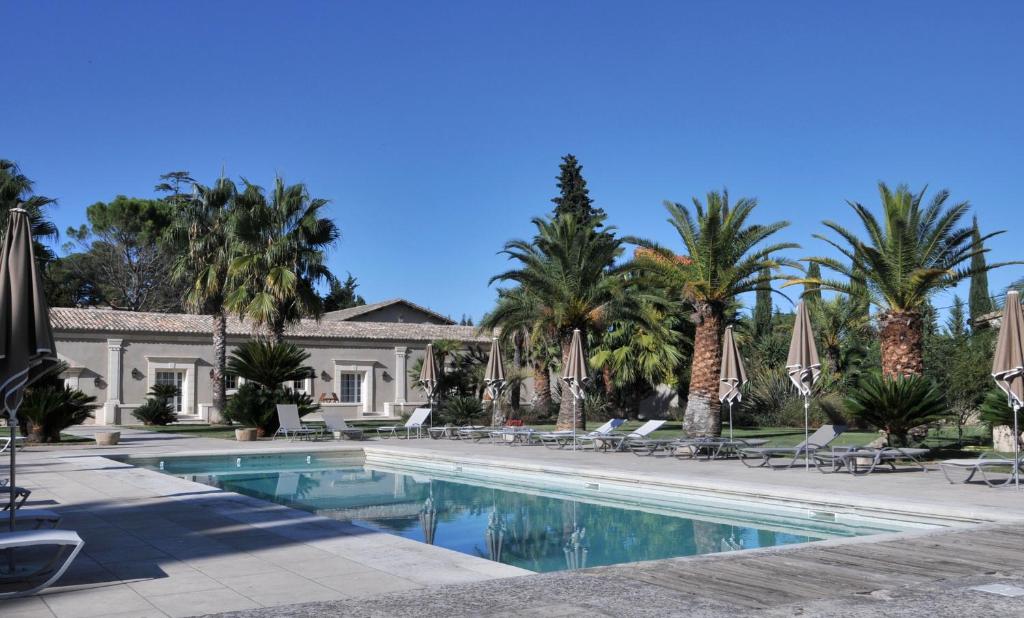 a swimming pool with umbrellas and palm trees at Domaine du Grand Malherbes in Aimargues