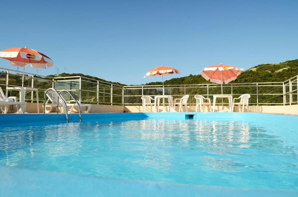 a swimming pool with chairs and umbrellas at Joaquina Beach Hotel in Florianópolis