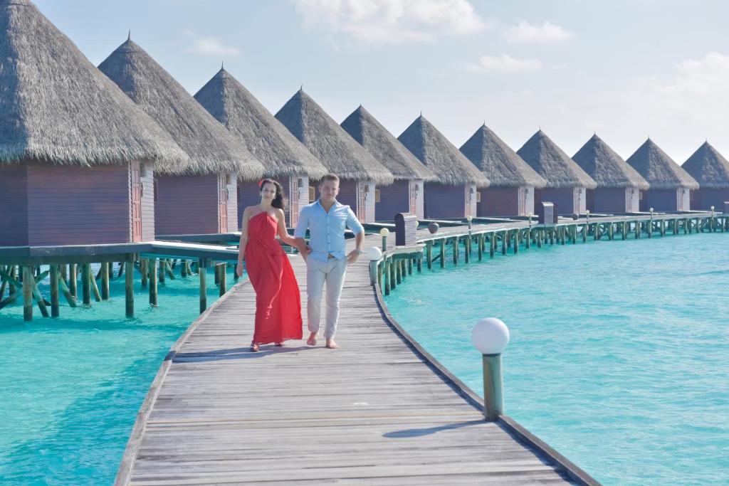 a man and woman walking on a wooden bridge over the water at Thulhagiri Island Resort & Spa in North Male Atoll