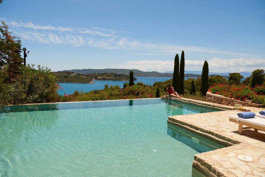 a swimming pool with a man sitting on a bench next to a lake at Beachfront Villa in Porto Heli