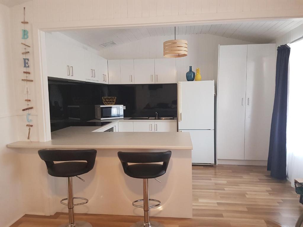 eine Küche mit weißen Schränken und einer Theke mit zwei Barhockern in der Unterkunft Dells Seaside Escape Moonta Bay in Port Moonta