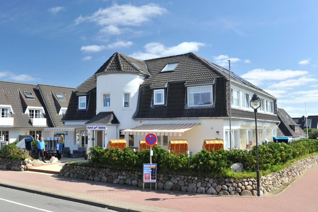 a large white house with a black roof on a street at Hotel Hansa in Wenningstedt