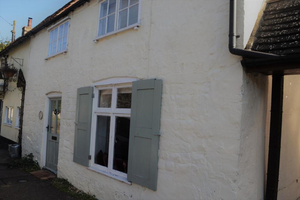 a white building with green shutters and a window at Bell Cottage in Mildenhall
