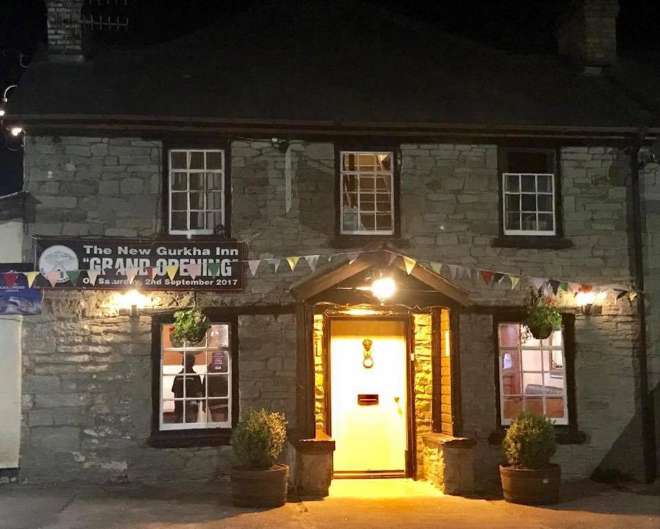 a stone building with a white door at night at New Gurkha Inn in Brecon