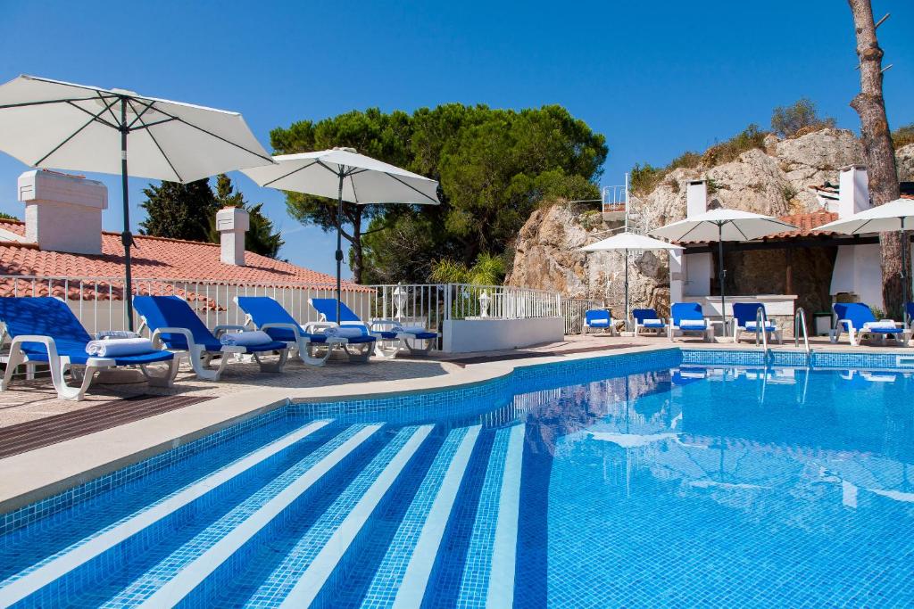 a swimming pool with blue chairs and umbrellas at Villa Branca do Castelo in Sesimbra