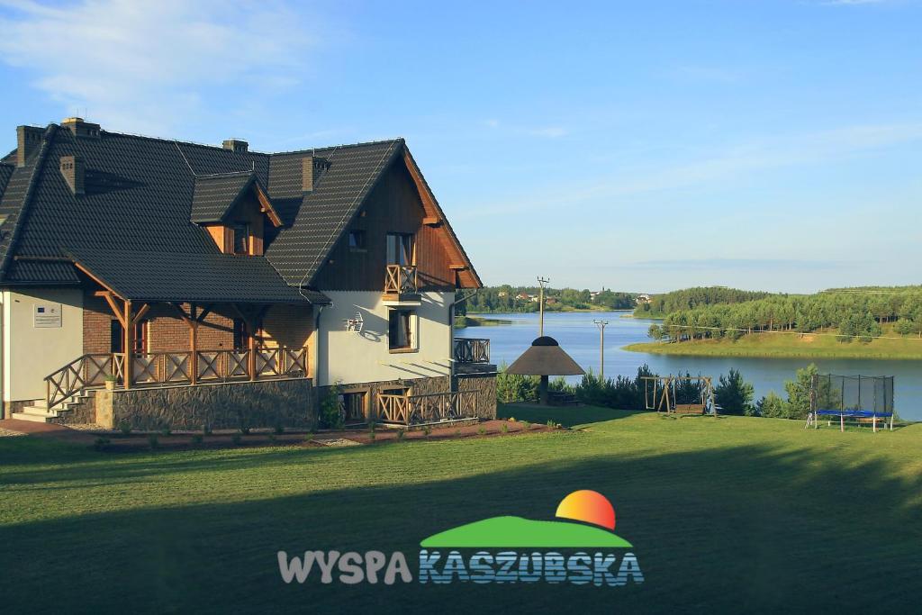 ein Haus auf einem Rasen neben einem See in der Unterkunft Wyspa Kaszubska dom wypoczynkowy z sauną i balią in Lipnica