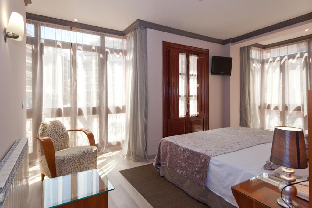a bedroom with a bed and a chair and windows at Hotel Vetusta in Oviedo